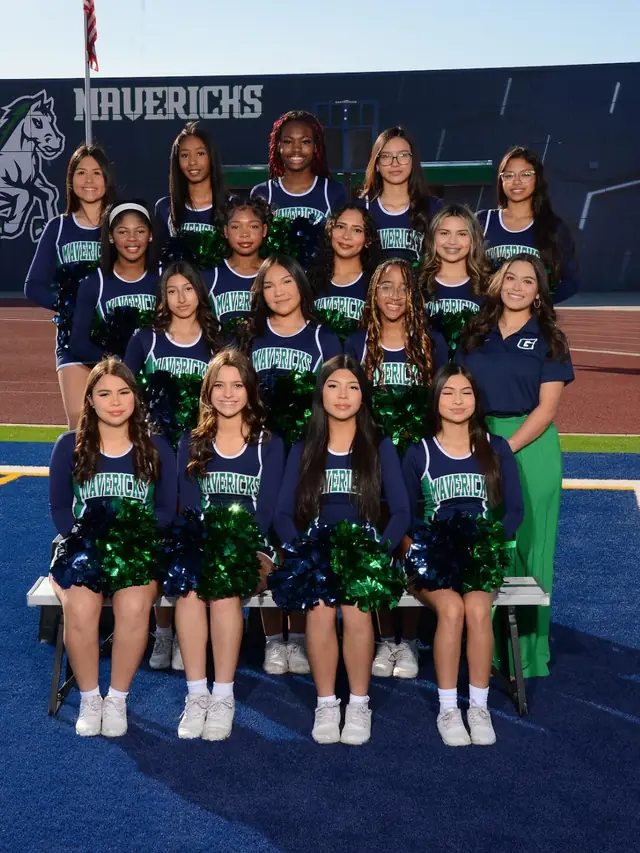 The squad seated with poms in front of the Mavericks wall at the stadium