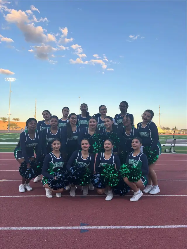 The squad kneeling with poms on the track at dusk