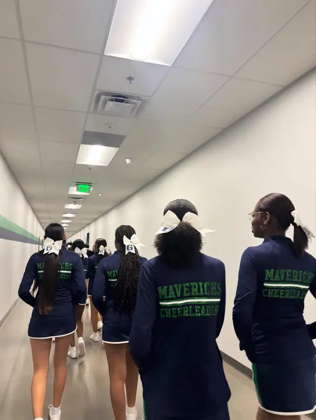 Cheerleaders in navy Mavericks Cheerleading jackets walking down a hallway