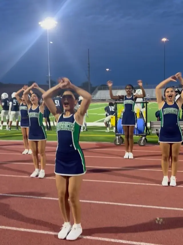 A Goodyear cheerleader mid-motion on the track under the stadium lights